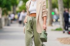 an edgy outfit with a white crop top, a tan oversized blazer, green joggers, white strappy shoes, a green mini bag