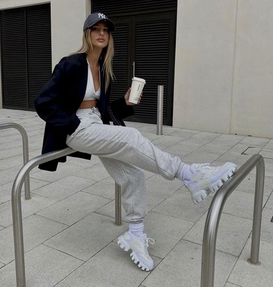 grey joggers, white sneakers and socks, a white bra top, an oversized black blazer and a black baseball cap