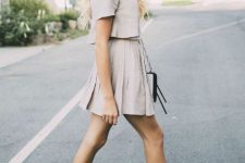 With beige crop shirt, sunglasses, beige pleated mini skirt and light gray and black chain strap bag