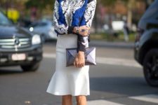With black, white and cobalt blue printed shirt, silver necklace, sunglasses, white knee-length skirt and black ankle strap high heels