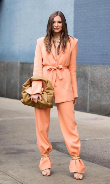 With golden necklace, peach colored belted long blazer, peach colored loose pants and brown leather bag