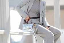 With gray fitted turtleneck, light gray long blazer, light gray pants, black and white leather lace up flat shoes, black leather belt and mirrored rounded sunglasses