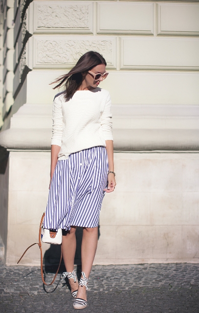 With white loose sweatshirt, beige framed oversized sunglasses, white and navy blue striped button front knee-length skirt and white and brown bag