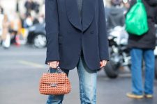 a Parisian chic look with a grey turtleneck, an oversized black blazer, blue jeans, black boots and an orange bag
