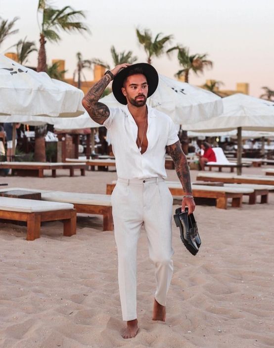 a beach look with a white short-sleeved button down, neutral pants, black loafers and a black hat