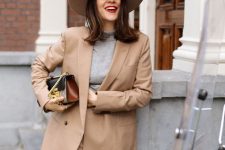 a beige pantsuit with an oversized blazer, a grey turtleneck, a wide-brim hat and a chic printed mini bag