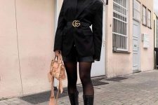 a black turtleneck, black shorts, an oversized black blazer with a belt, black chunky boots and a neutral bag for a touch of color