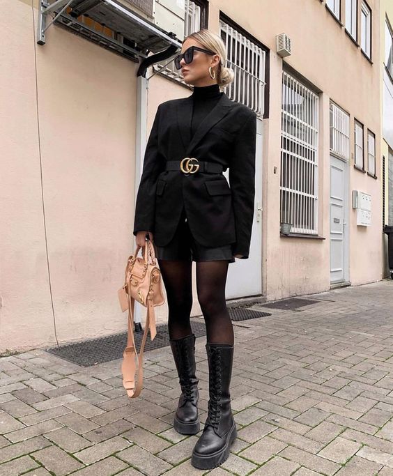 a black turtleneck, black shorts, an oversized black blazer with a belt, black chunky boots and a neutral bag for a touch of color
