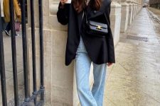 a casual outfit with a white t-shirt, blue flare jeans, black sneakers, an oversized black blazer and a black bag