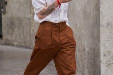 a fashionable outfit with a white oversized button down, rust-colored cuffed trousers, black loafers and a neck tie