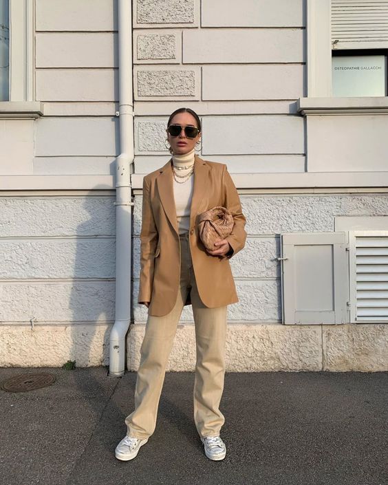a neutral turtleneck, tan jeans, white sneakers, an oversized camel blazer and a camel woven bag plus layered necklaces