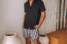 a relaxed monochromatic summer look with a black short-sleeved shirt, black and white striped shorts, black flipflops and a hat