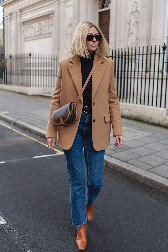 a timeless outfit with a black turtleneck, blue cropped jeans, brown boots, a camel blazer and a chic saddle bag
