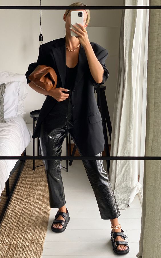 a total black look with a top, leather pants, an oversized black blazer, black sandals and a brown clutch