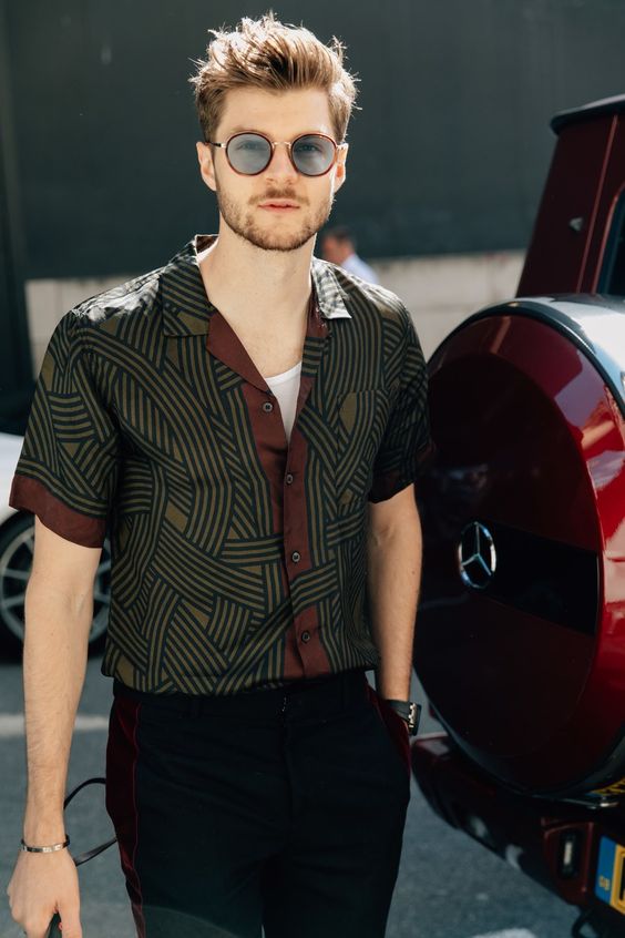 a trendy outfit with a white tank top, a dark printed shirt, black trousers and grey sunglasses is a cool idea for spring or fall