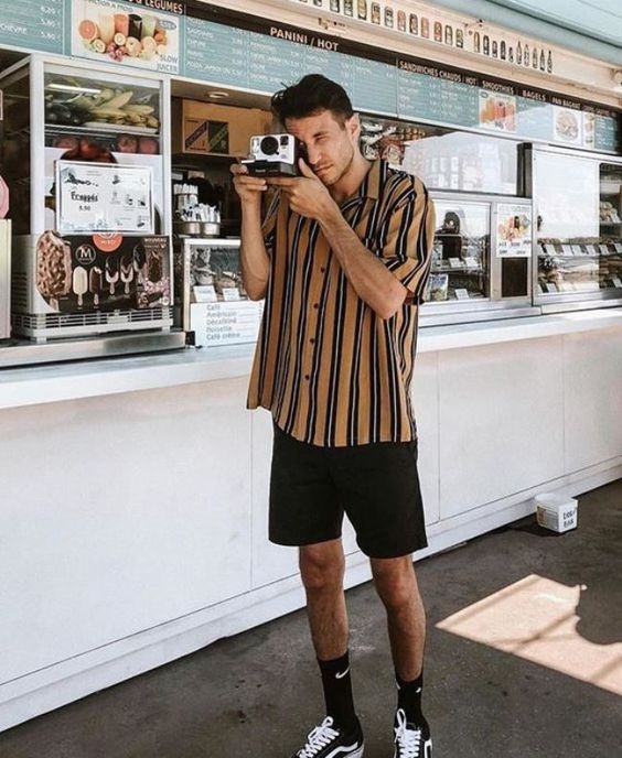 a vacation outfit with a beige and black striped shirt, black shorts, black socks and black sneakers is retro inspired and cool