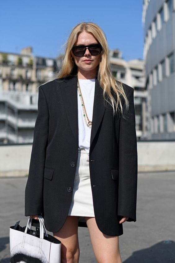 a white shirt, a white leather mini, an oversized black blazer, layered necklaces and a white tote for a spring to summer look