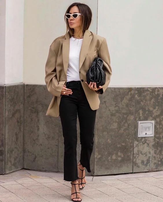 a white t shirt, black cropped jeans, black strappy heels, an oversized beige blazer and a black woven clutch and cat eye sunglasses