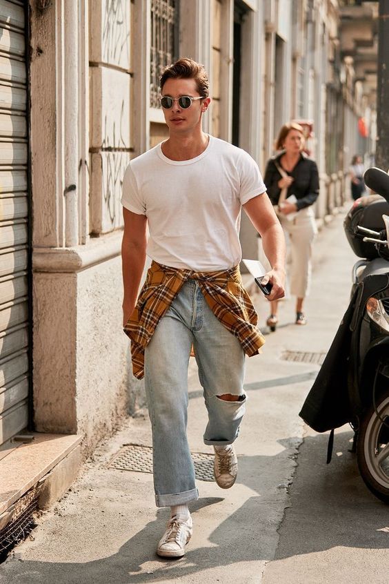 a white t-shirt, blue ripped jeans, white sneakers and socks and a mustard checked shirt and sunglasses