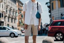 a white tee, a white short-sleeved shirt, tan shorts, white socks and grey trainers, a turquoise mini bag