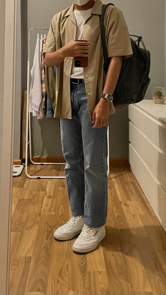 an every day spring outfit with a white t shirt, a beige short sleeved shirt, blue jeans, white sneakers and a black backpack