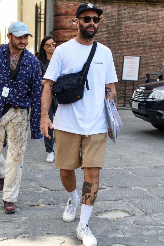 an oversized white t-shirt, tan shorts, white sneakers and socks plus a black bag and a black baseball cap
