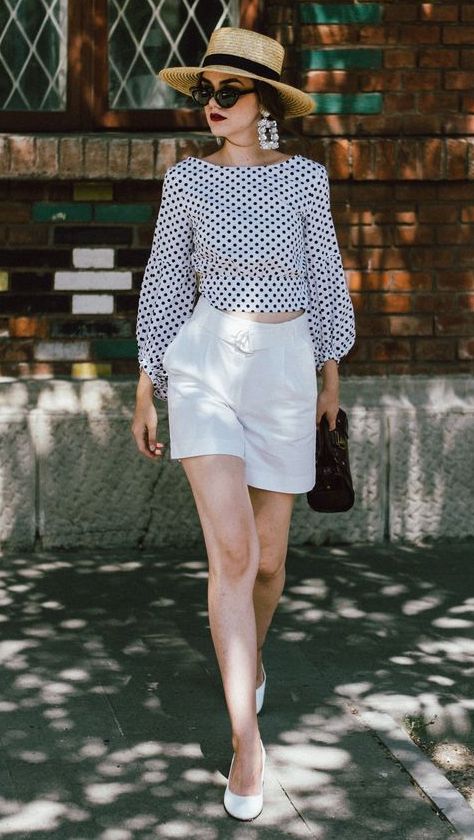 a black and white crop top with long sleeves, white high waisted shorts, white shorts, a straw hat and a black bag