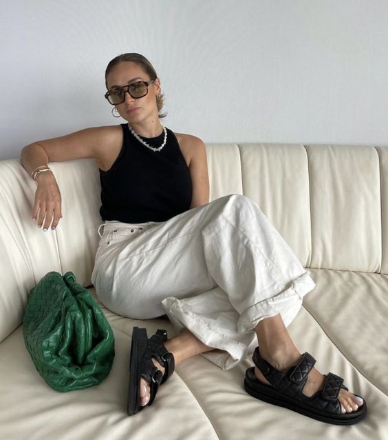 a black and white outfit with a black halter neckline top, white jeans, black birkenstocks and a green clutch plus a necklace