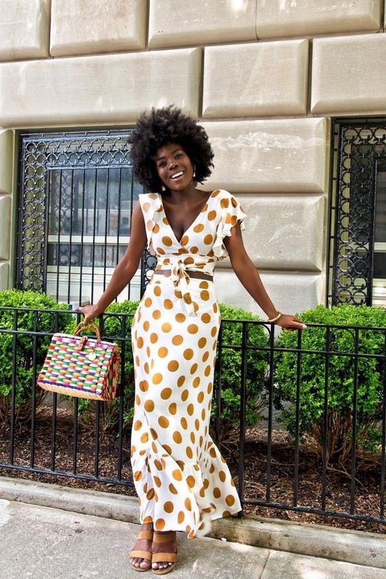a fitting polka dot maxi dress with a deep neckline and one shoulder, a brown belt, yellow strappy shoes and a colorful box bag