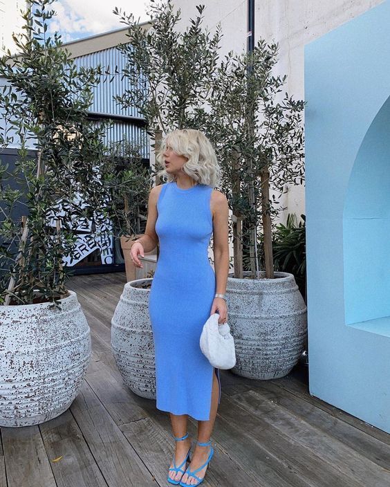 a Very Peri sleeveless midi dress with a side slit, blue strappy shoes and a white bag are a great and chic combo for work