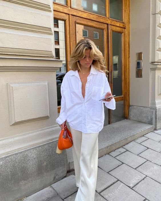 a casual outfit with an oversized white shirt, neutral pants, white sneakers and an orange bag is a lovely look for summer