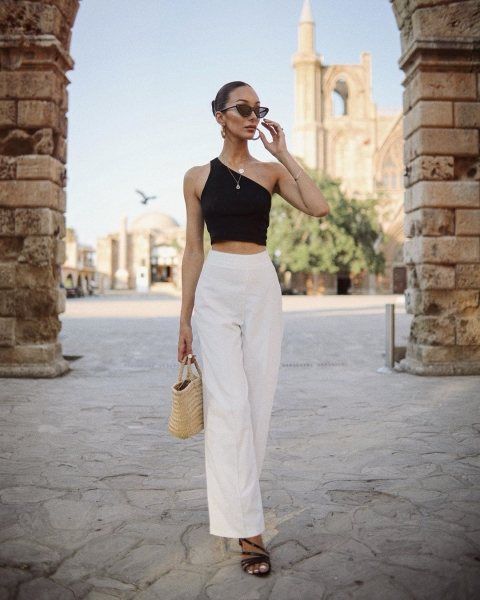 a black asymmetrical crop top, white high waisted pants, black strappy shoes and a woven bag plus layered necklaces