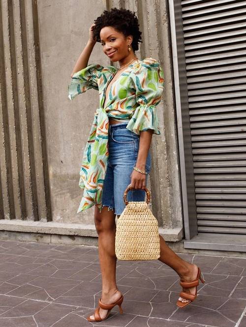 a bright tied up statement blouse with puff sleeves, blue denim shorts, brown heels and a woven bag with round handles