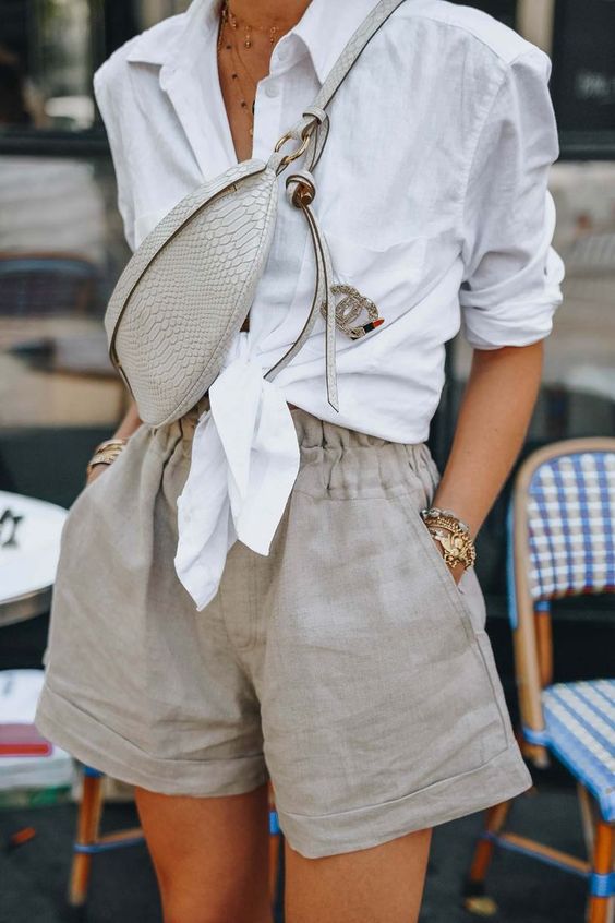 a casual brunch outfit with a white tied up shirt, grey linen shorts with pockets, a grey waistbag and layered necklaces for a hot day