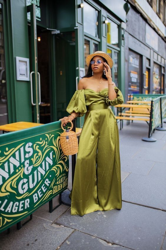 a green suit off the shoulder jumpsuit with palazzo pants and puff sleeves, a straw bag and a straw hat and statement earrings
