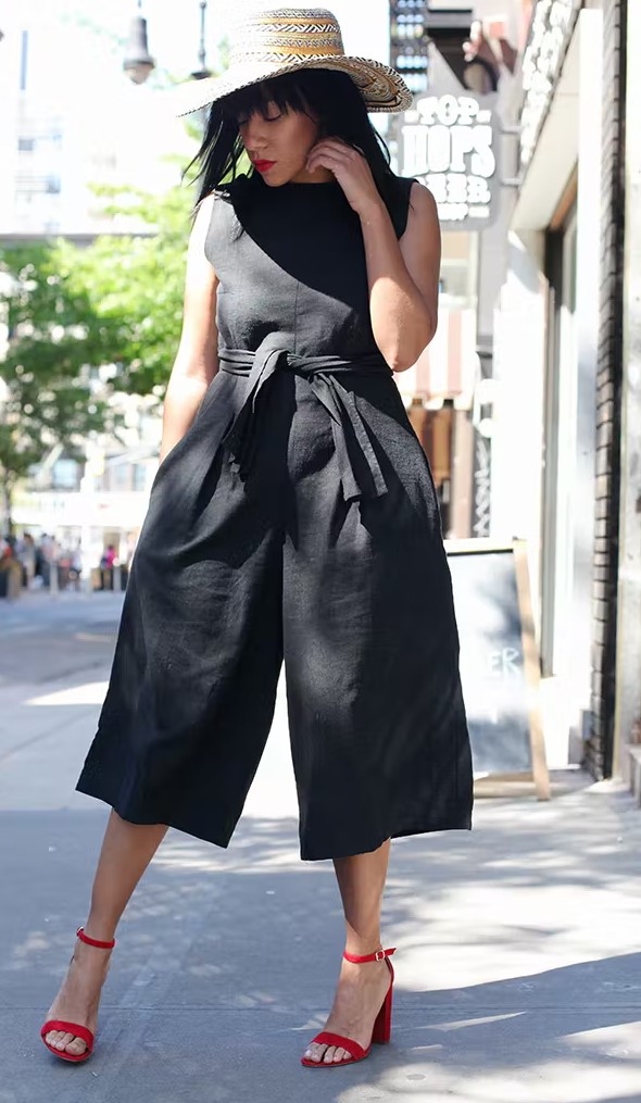 a black sleeveless cropped jumpsuit with wideleg pants, pockets and a sash, a printed hat and red block heels is amazing