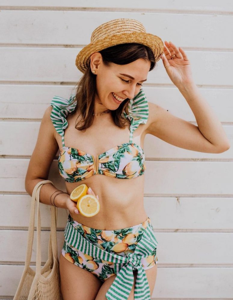 a retro chic swimsuit with a cutout bra with ruffles and a high waisted bottom with a sash, a straw hat and a woven bag