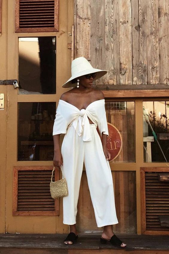 a refined look with an off the shoulder tied up, high waisted pants, black slides, a hat and a woven mini bag and statement earrings