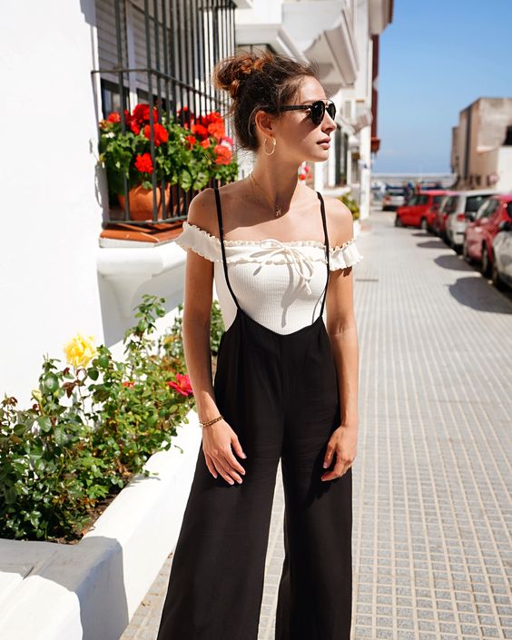 a white off the shoulder ruffle top plus a black spaghetti strap overall and gold hoop earrings are a simple look with a Mediterranean feel