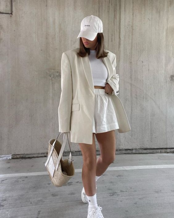 a white crop top, white shorts, white socks and trainers, a creamy oversized blazer, a white baseball cap and a straw bag