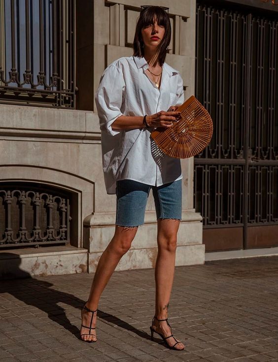 an oversized white shirt, blue denim biker shorts, black strappy heels and a wooden bag for a lovely summer outfit