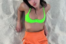 Dua Lipa wearing a neon green swimsuit top and an orange overall to the beach looks super bold and absolutely amazing