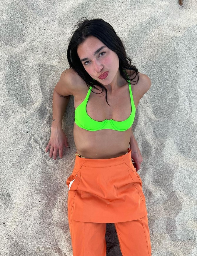 Dua Lipa wearing a neon green swimsuit top and an orange overall to the beach looks super bold and absolutely amazing