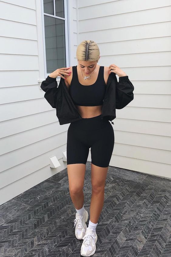 Kylie Jenner wearing a black bra top, biker shorts, white socks and trainers and a black cropped hoodie with a zip