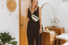 a black linen jumpsuit with a V-neckline and no sleeves, black heels and a neutral waistbag are a simple and comfy summer look