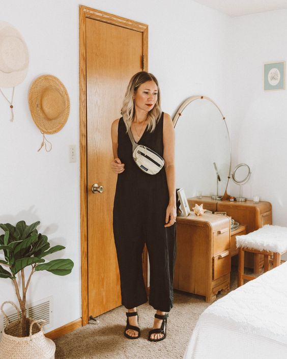 a black linen jumpsuit with a V neckline and no sleeves, black heels and a neutral waistbag are a simple and comfy summer look