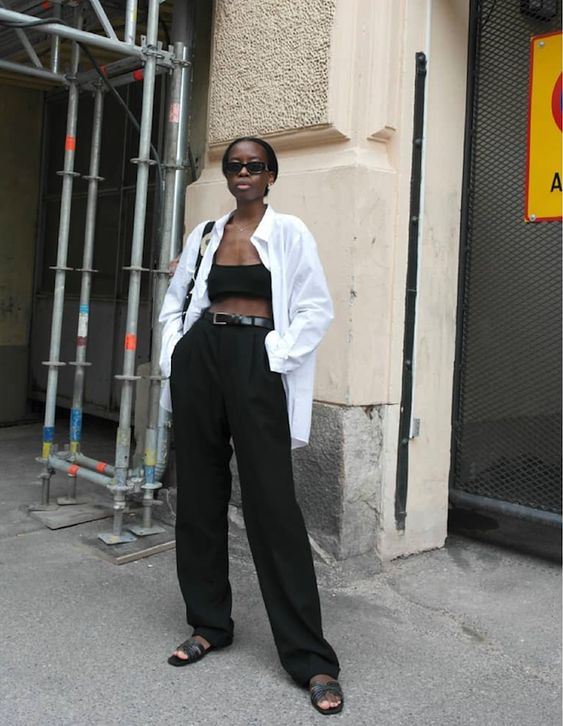 a contrasting summer outfit with a bra top, high waisted wideleg trousers, black slides, an oversized white shirt, a black bag