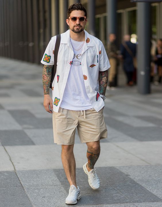 a layered look with a white printed t-shirt, a white printed shirt, tan shorts, white sneakers and a black bag is great for summer