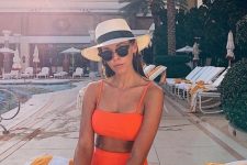 a neon orange swimsuit with a square neckline bra top and a high waisted bottom plus a straw hat and classic sunglasses