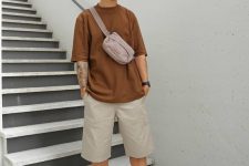 a neutral summer look with a brown oversized t-shirt, grey Bermuda shorts, white sneakers and socks, a bucket hat and a waist bag